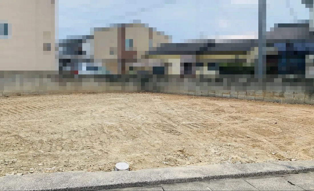 解体して整地された更地。手前に道路と側溝、敷地の境界にブロック塀がある